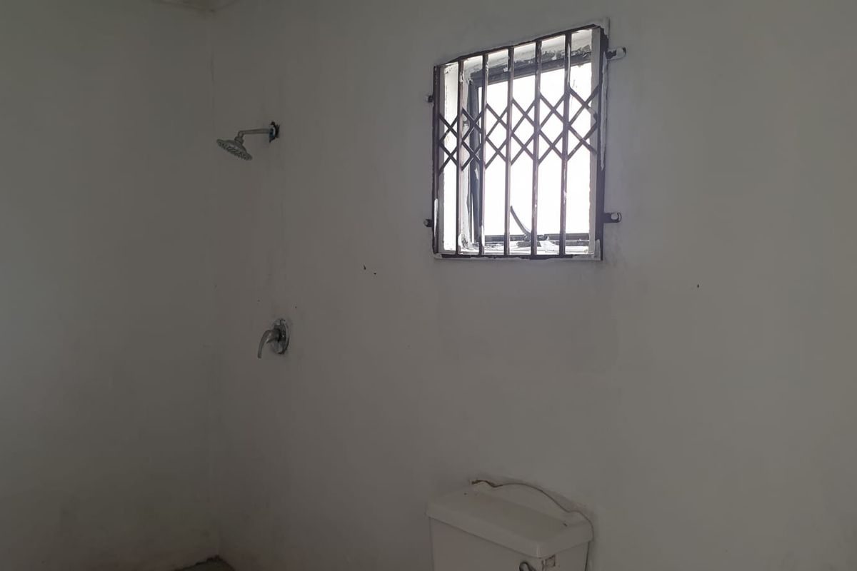 A basic bathroom featuring a shower head, toilet, and a window with security bars, requiring renovation and cosmetic updates.