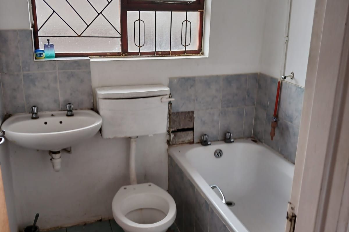 A dated bathroom featuring a standard bathtub, wall-mounted basin, and toilet, with visible wear to the tiling and wall finishes.