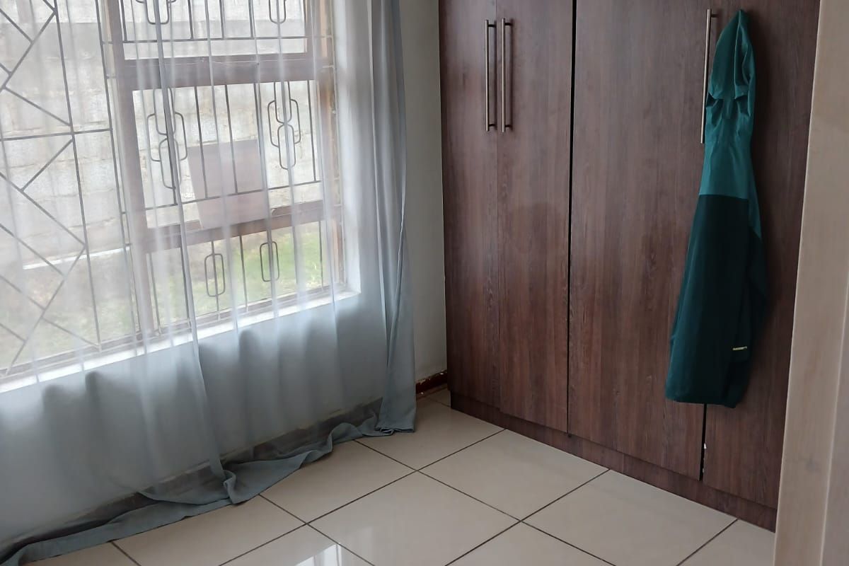 A bedroom featuring large built-in wooden wardrobes, tiled flooring, and a window fitted with security bars.