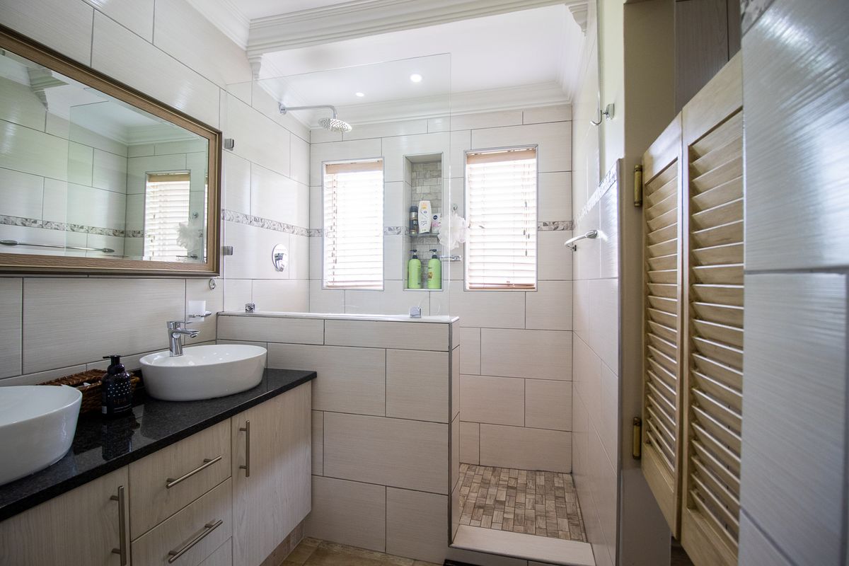 Modern bathroom featuring a double vanity with granite countertop, walk-in shower with glass screen, recessed niche, and neutral tiled finishes.