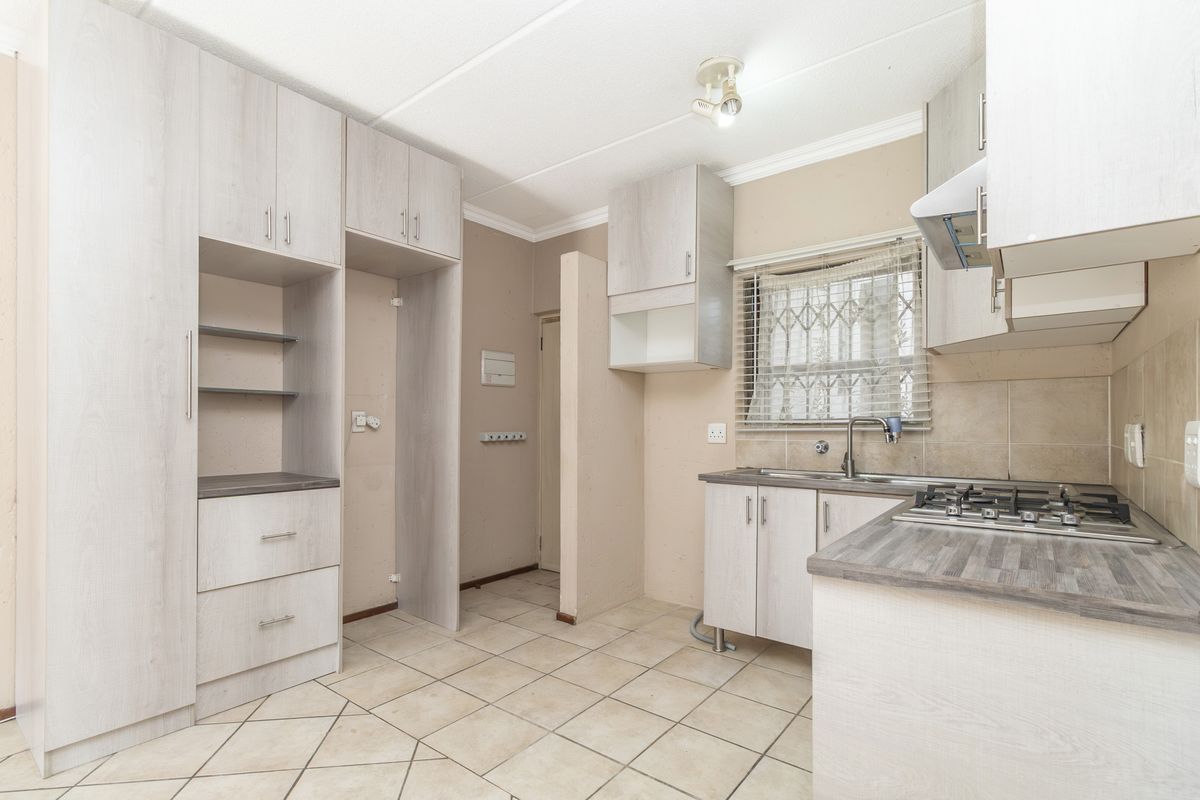 A functional kitchen featuring light-toned built-in cabinetry, laminate countertops, a gas hob with extractor fan, and tiled flooring.