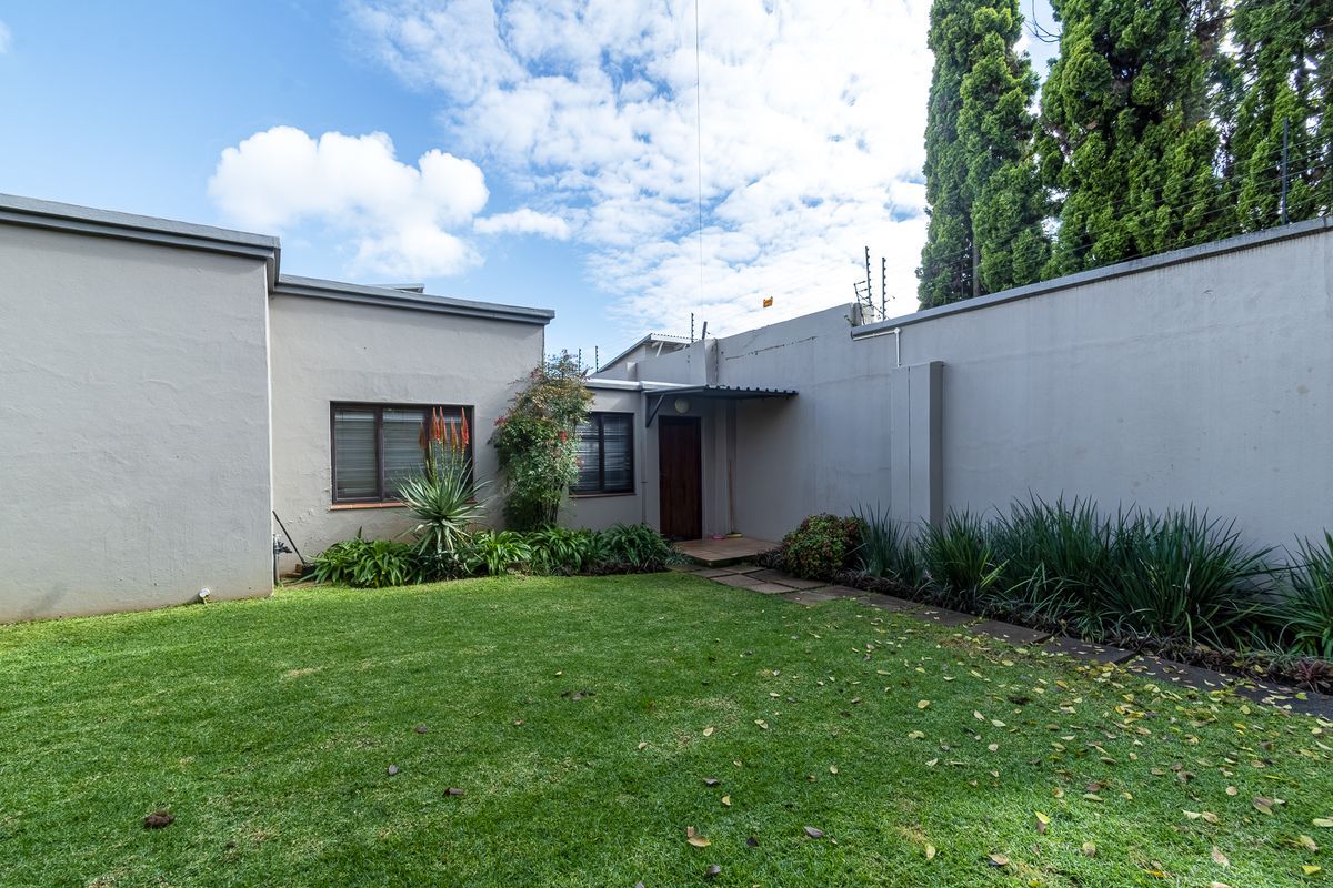 Rear exterior view of the property featuring a private lawn, perimeter wall with electric fencing, and a small paved entrance area.