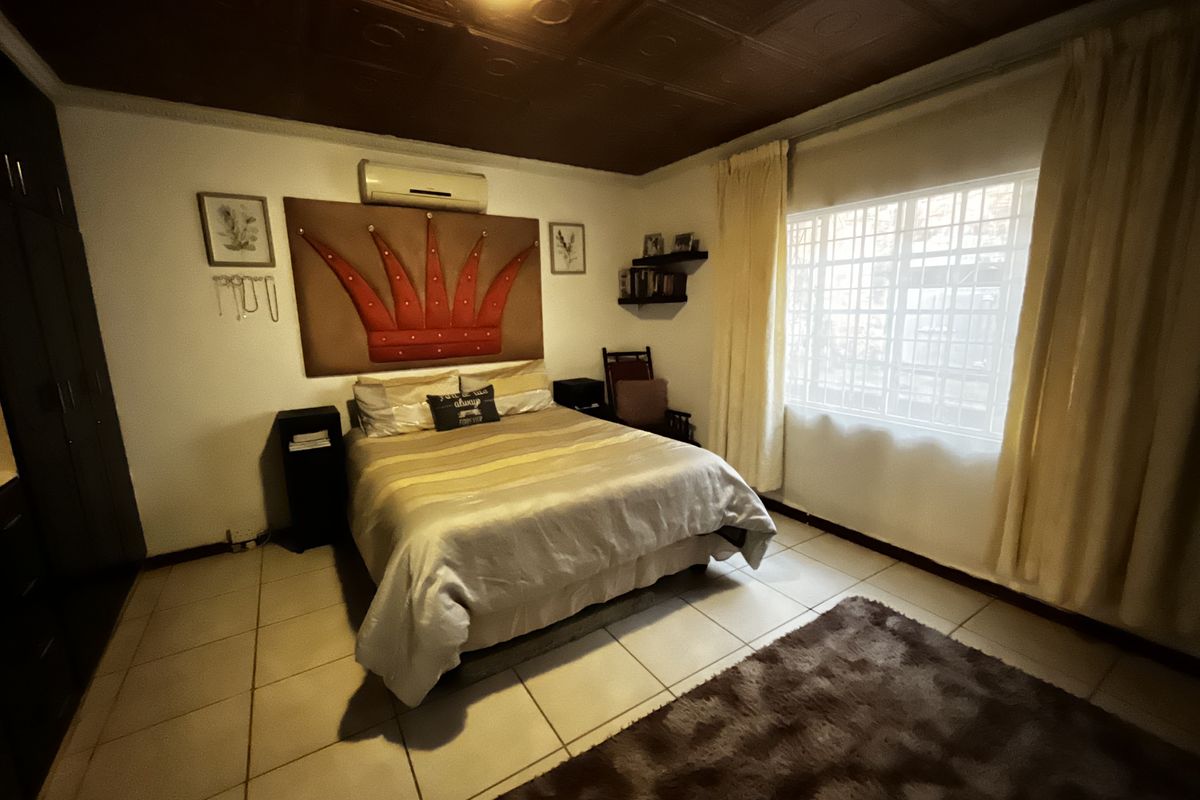 A bedroom featuring tiled flooring, a decorative coffered ceiling, built-in cupboards, and a wall-mounted air conditioning unit.