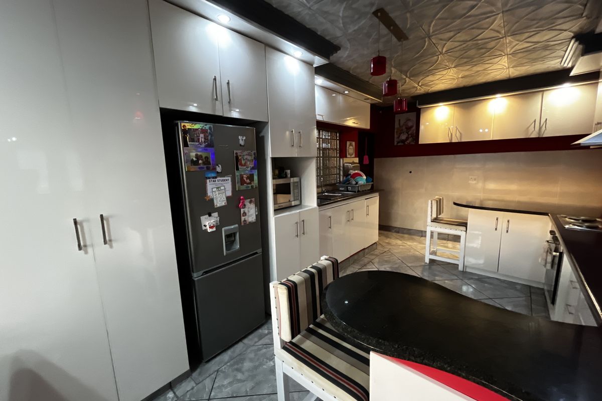 Modern kitchen featuring high-gloss white cabinetry, dark granite countertops, integrated appliances, and a breakfast bar area with decorative ceiling finishes.