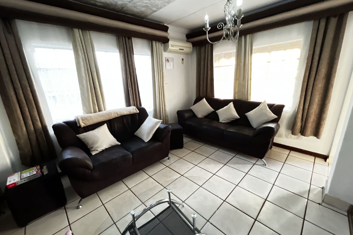 A living room featuring tiled flooring, a wall-mounted air conditioning unit, and a decorative chandelier.