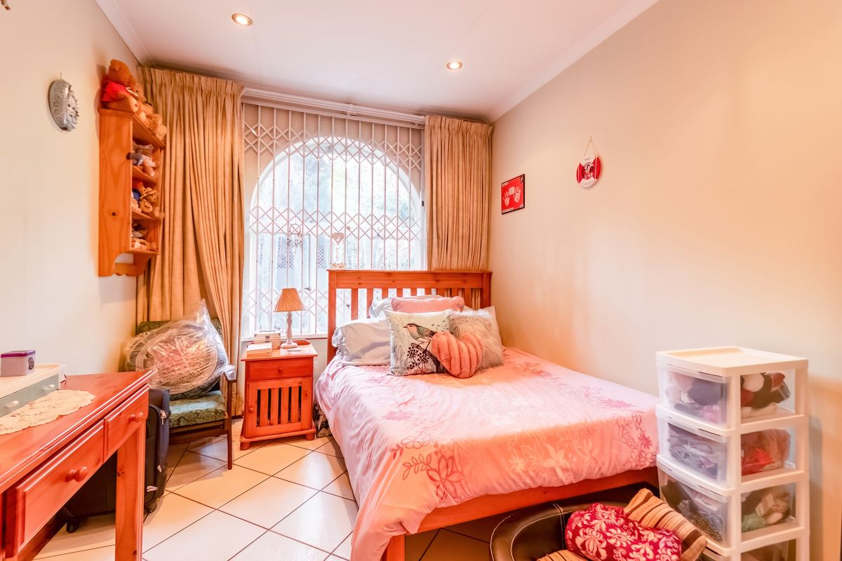 A cozy bedroom featuring tiled flooring, recessed downlighting, and a large arched window secured with a metal security gate.