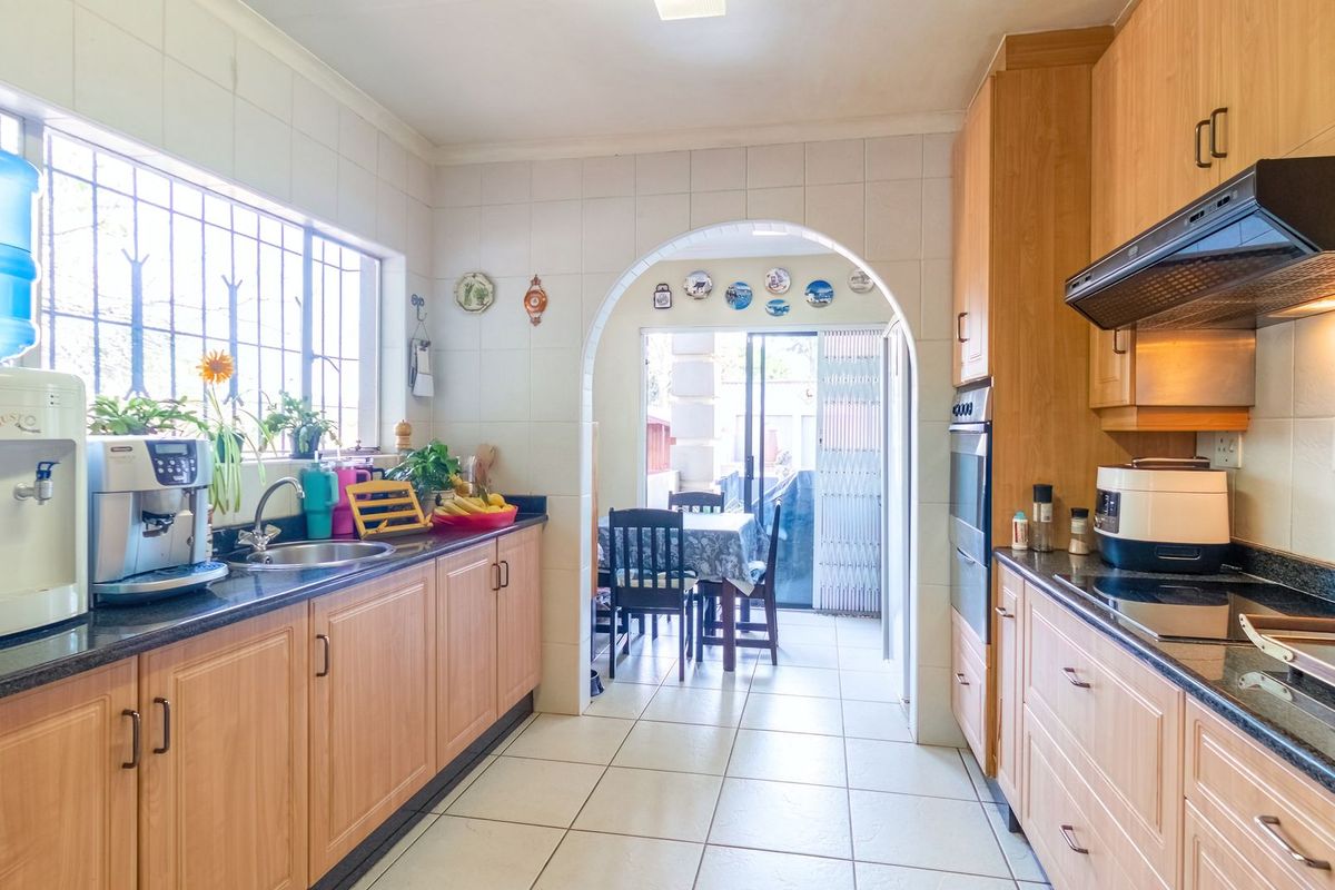 A functional kitchen featuring light wood cabinetry, granite countertops, built-in oven, and extractor fan, with an arched opening leading to an adjacent dining area.