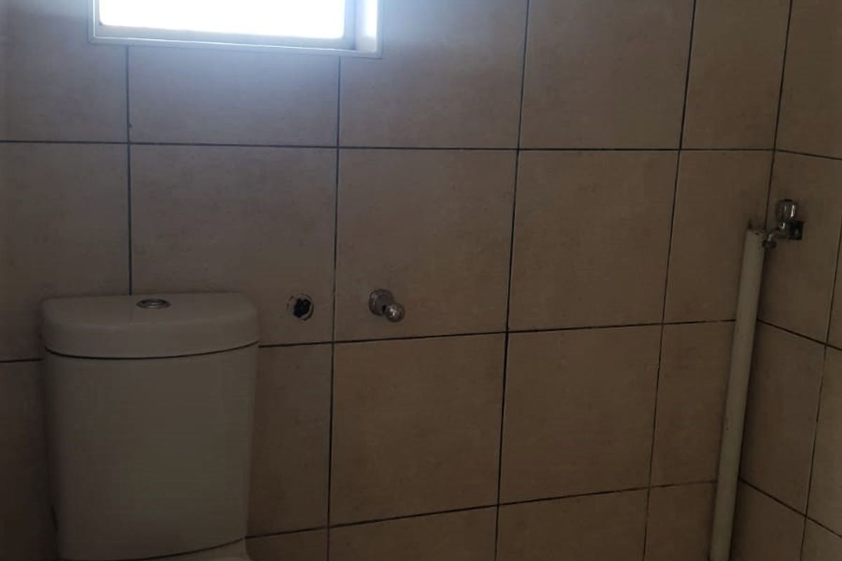 A compact bathroom featuring floor-to-ceiling wall tiles, a standard toilet, and an exposed water supply pipe.
