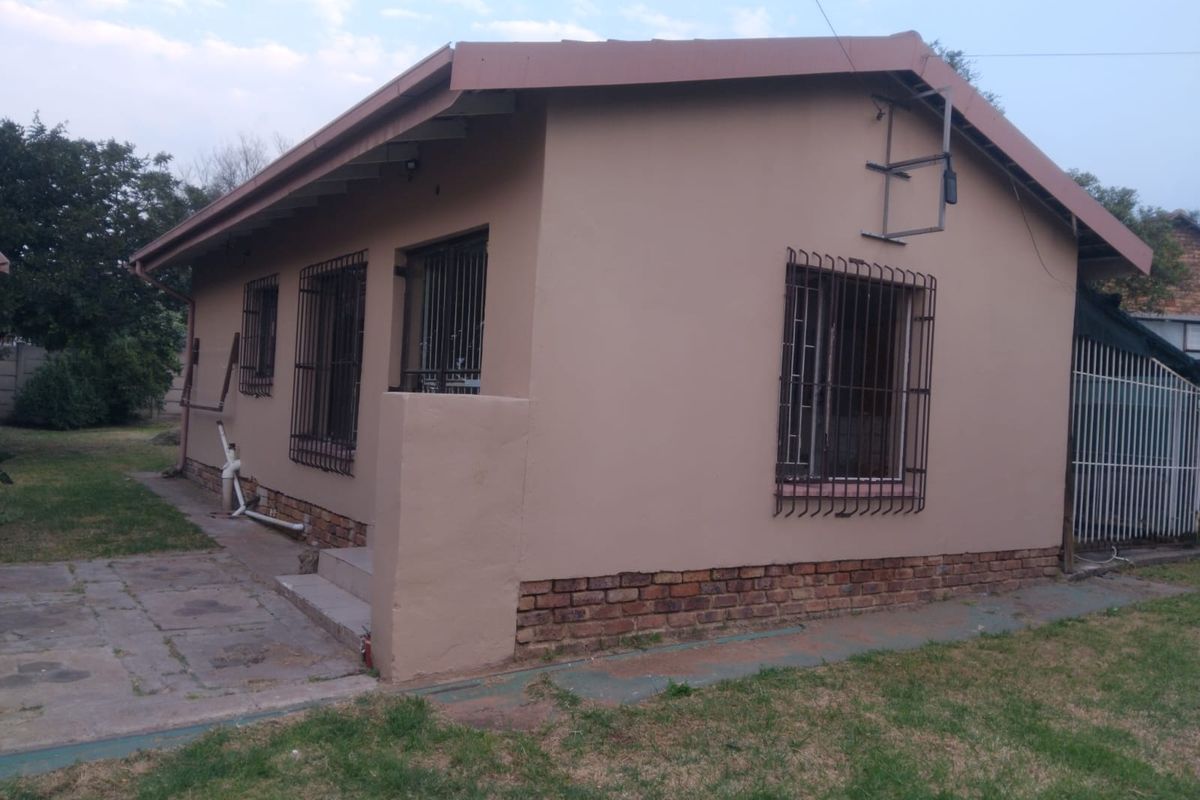 Rear view of the house featuring a paved patio area, security bars on windows, and a brick base foundation.