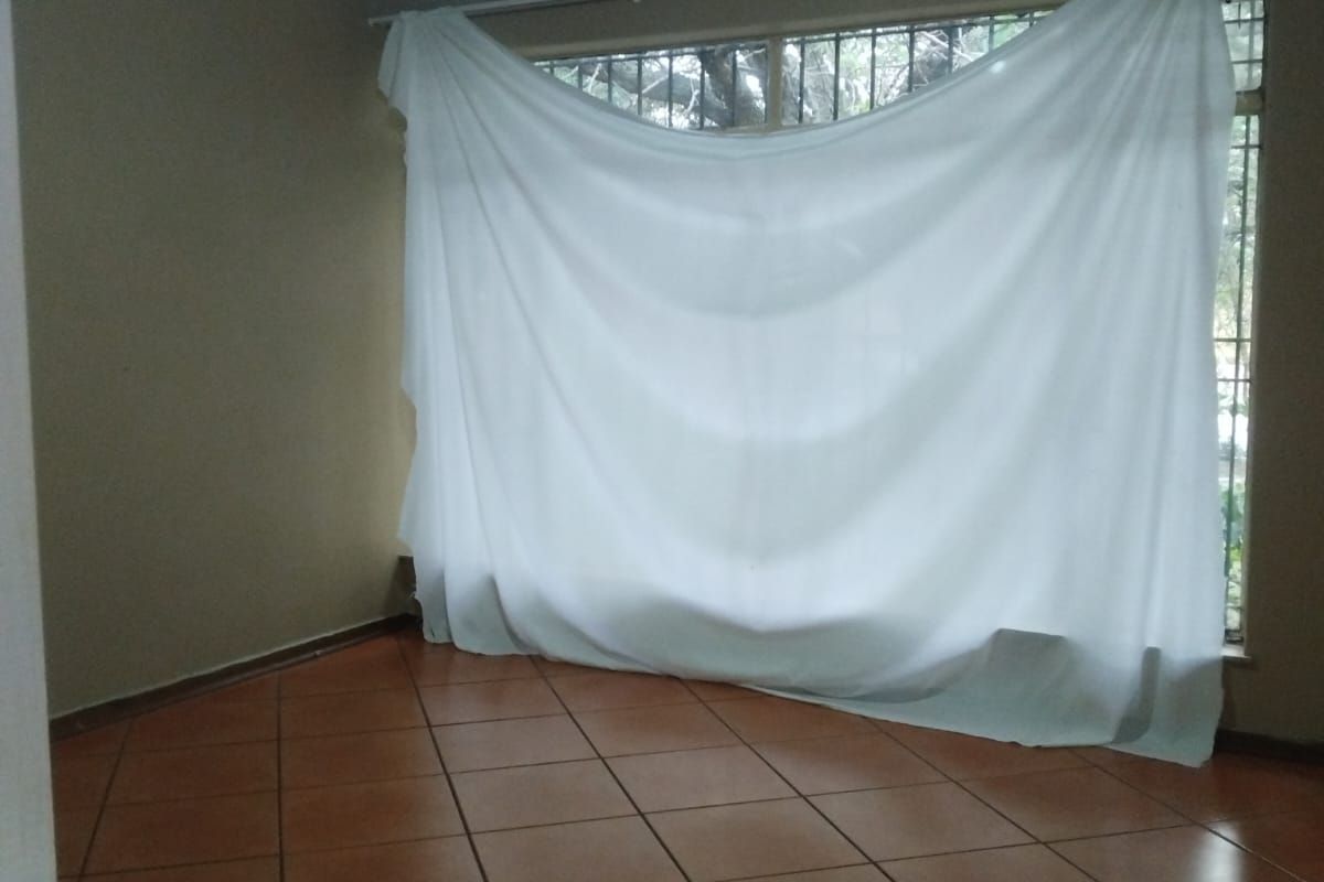 An empty bedroom featuring ceramic floor tiles, a timber ceiling, and security bars on the window.