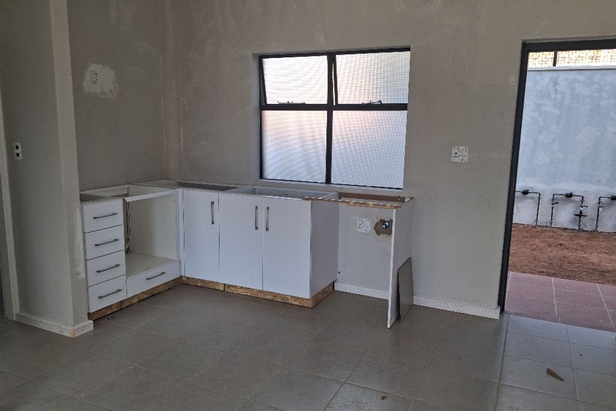 An unfinished kitchen area featuring base cabinetry, tiled flooring, and direct access to an outdoor space, requiring final finishes and appliance installation.