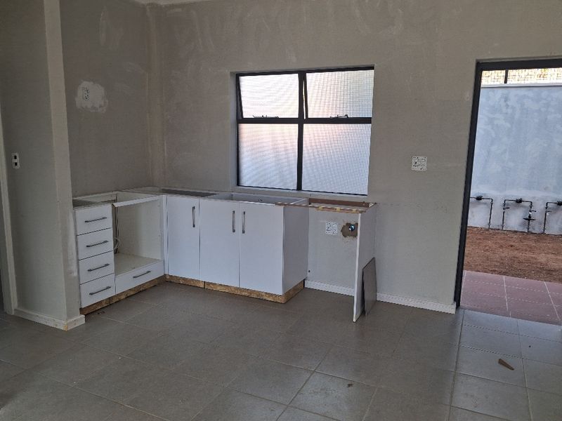 An unfinished kitchen area featuring base cabinetry, tiled flooring, and direct access to an outdoor space, requiring final finishes and appliance installation.