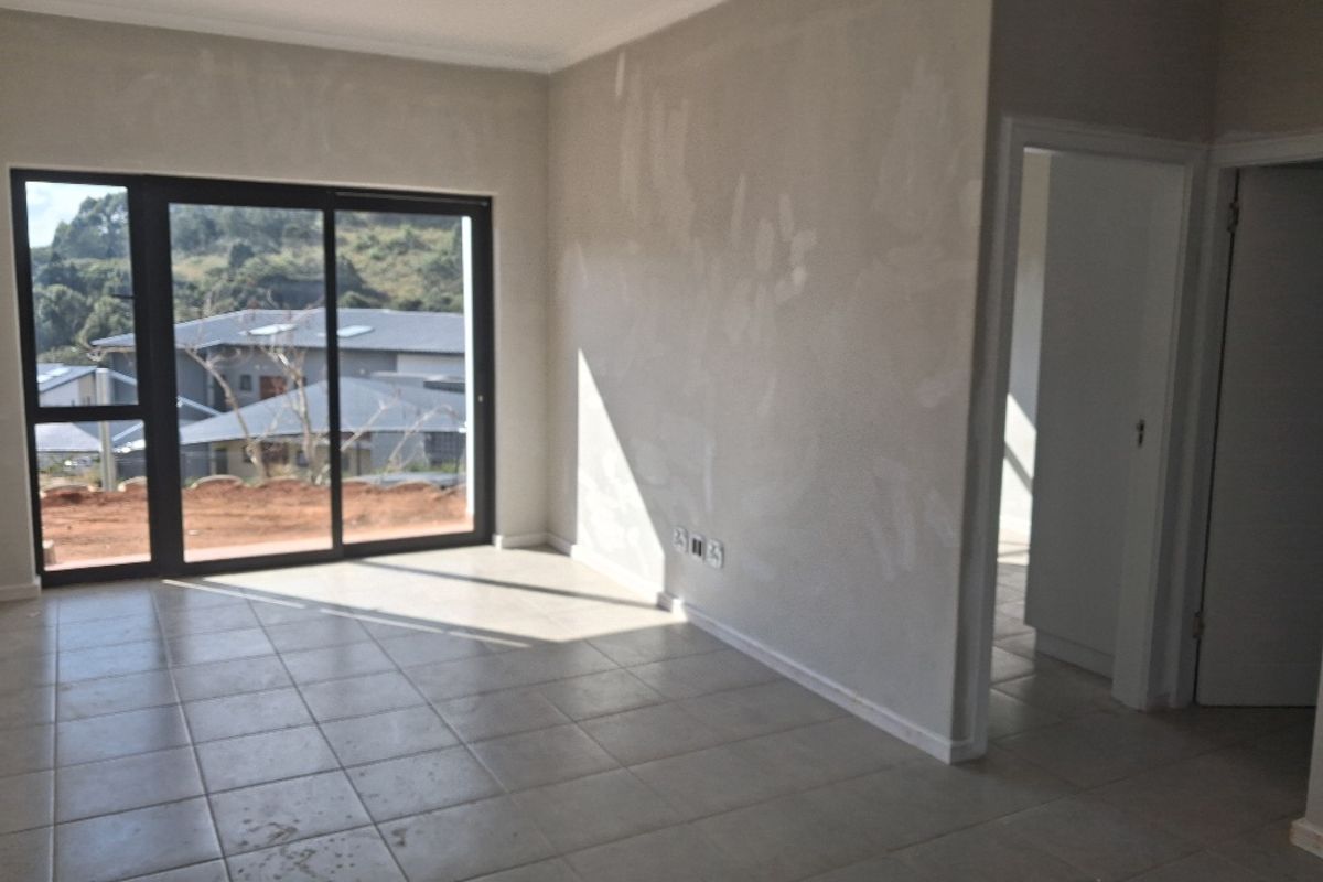 An empty living room featuring large sliding glass doors, ceramic floor tiles, and unfinished wall plaster, awaiting final painting and finishing touches.