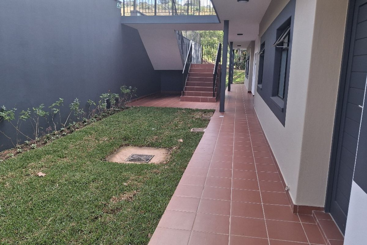 A well-maintained exterior rear walkway featuring tiled flooring, a staircase with metal railings, and a small adjacent garden area.