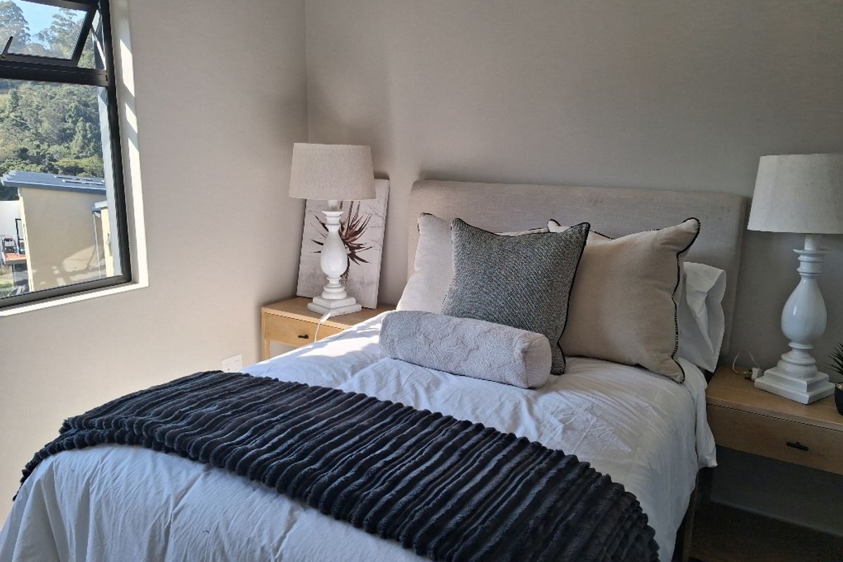 A well-lit bedroom featuring neutral wall tones and a modern aluminium window frame with views of the surrounding landscape.