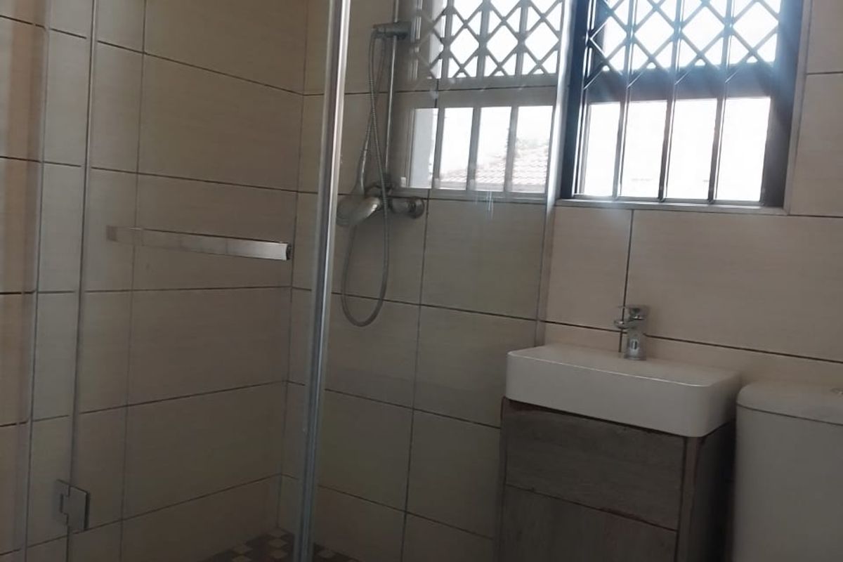 A compact bathroom featuring a glass-enclosed shower with a rainfall showerhead, a modern vanity basin, and a toilet with security bars on the window.