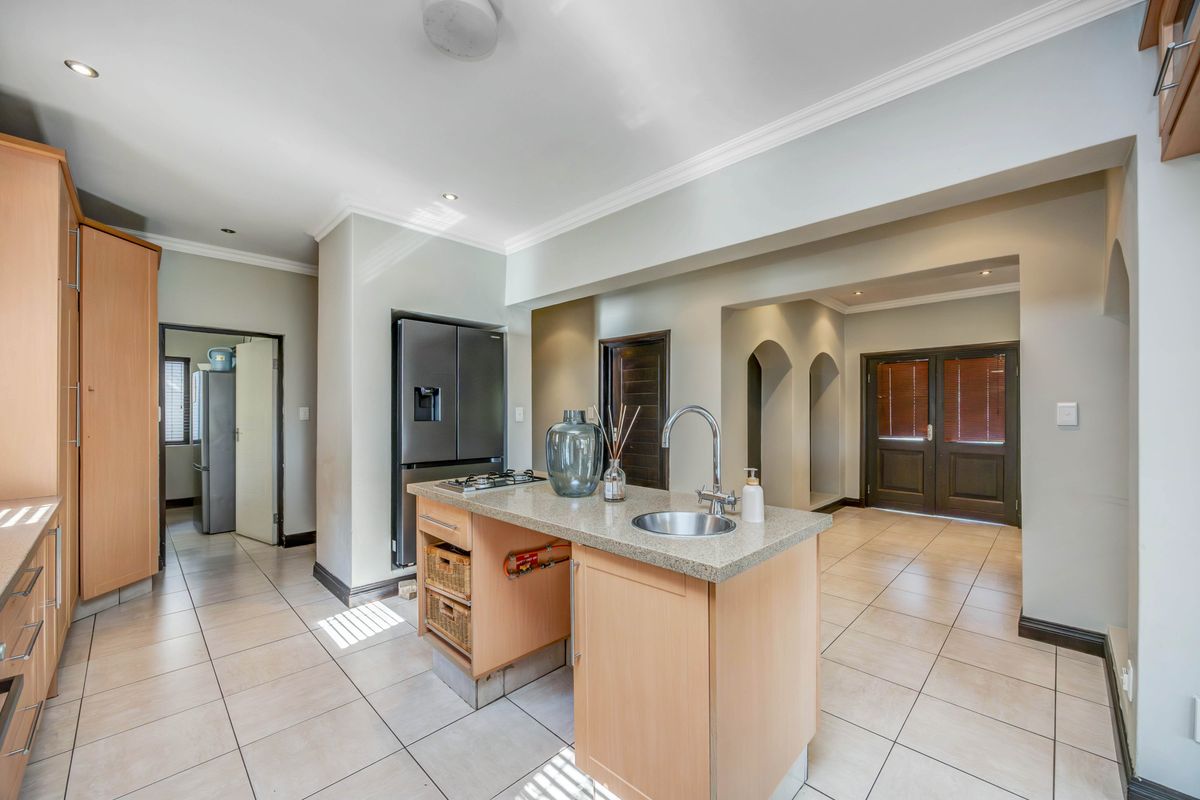 A functional kitchen featuring a central island with a stone countertop, gas cooktop, and tiled flooring, leading into an open-plan living area.