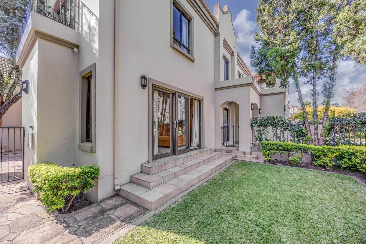 Rear view of the property featuring a landscaped garden, stone walkway, tiled patio steps, and sliding glass doors leading into the home.