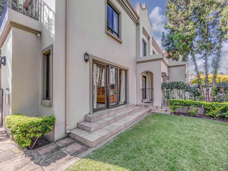 Rear view of the property featuring a landscaped garden, stone walkway, tiled patio steps, and sliding glass doors leading into the home.