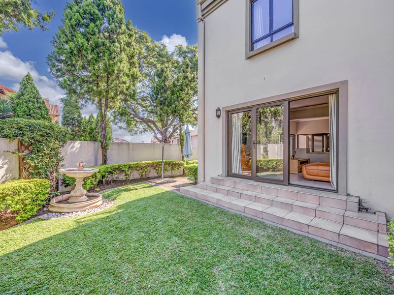 Rear view of the property featuring a tiled patio, sliding glass doors leading to the interior, and a well-maintained garden with a stone fountain.