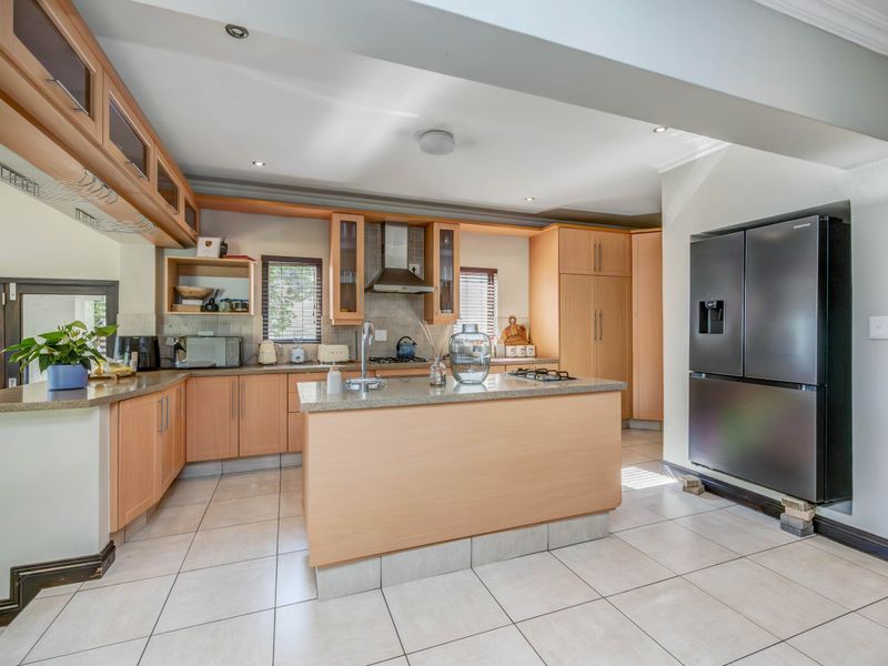 A functional kitchen featuring light wood cabinetry, stone countertops, a central island, and tiled flooring, providing a practical layout for cooking and preparation.