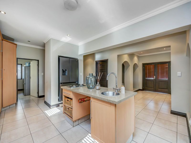 A functional kitchen featuring a central island with a stone countertop, gas cooktop, and tiled flooring, leading into an open-plan living area.