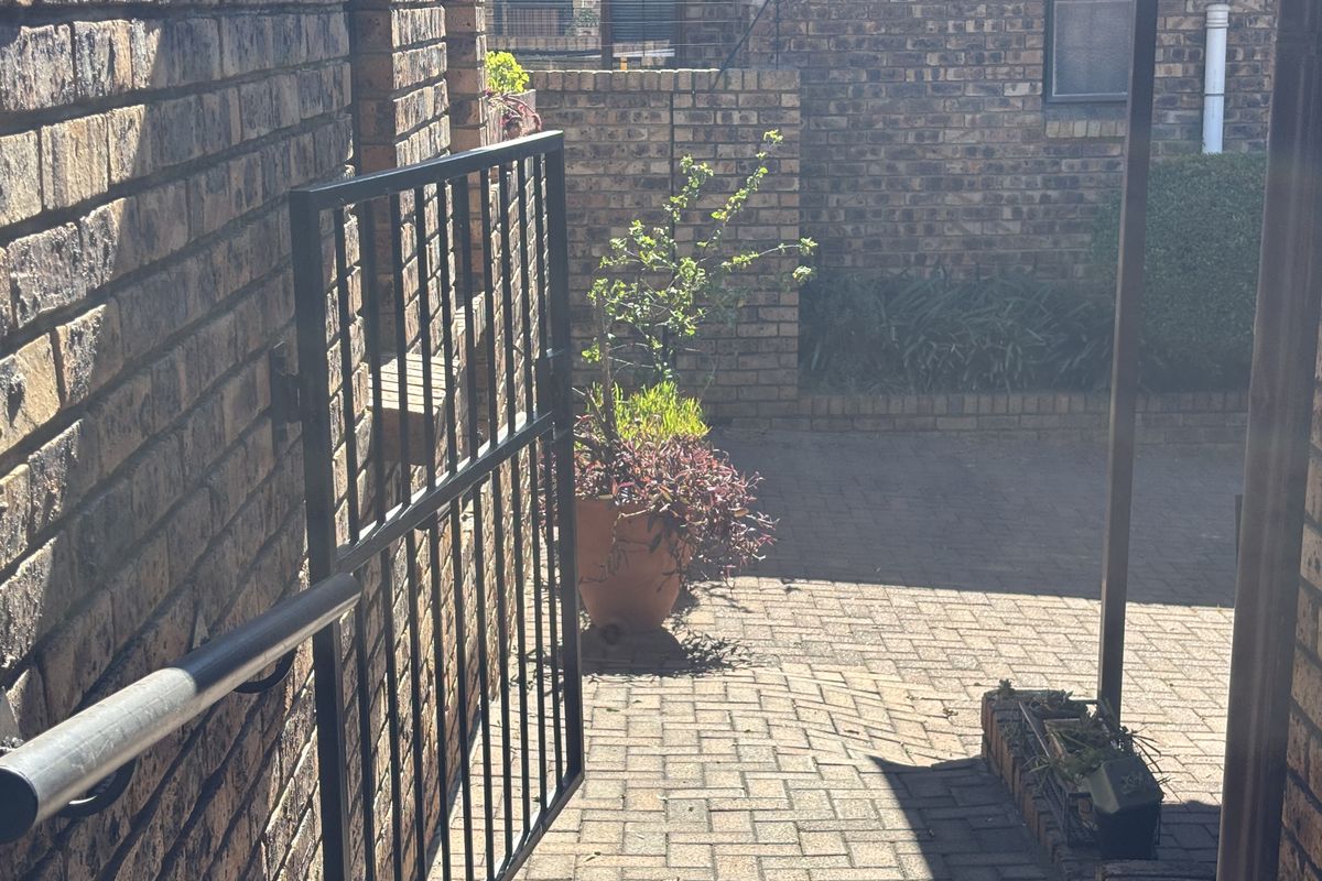 A private paved courtyard area featuring face-brick walls, a metal security gate, and a built-in brick planter box.
