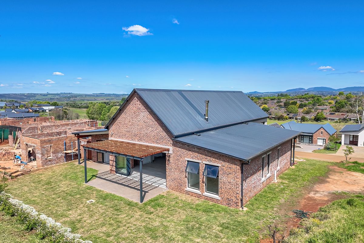 Aerial view of a modern brick house featuring a metal roof, covered patio with timber pergola, and landscaped garden area.