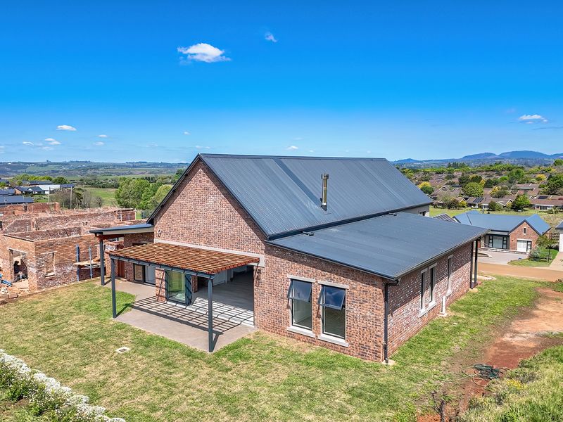 Aerial view of a modern brick house featuring a metal roof, covered patio with timber pergola, and landscaped garden area.