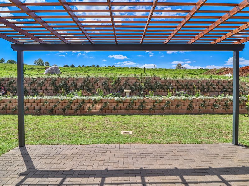 A well-maintained outdoor patio featuring a timber pergola, paved flooring, and a tiered retaining wall overlooking a landscaped garden.