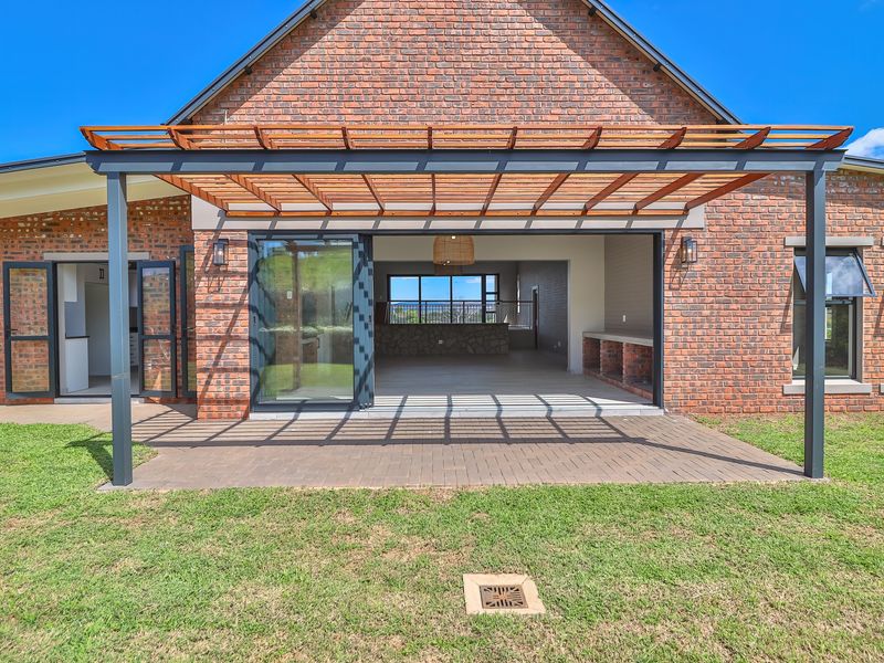 A spacious covered patio featuring a timber pergola, built-in braai, and seamless access to the interior through large stacking glass doors.