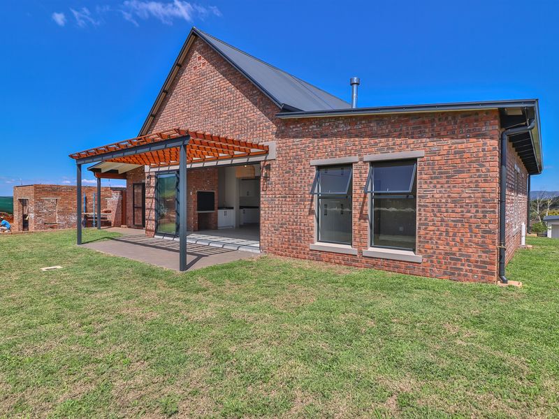 Rear view of a modern face-brick house featuring a covered patio with a timber pergola, built-in braai, and large aluminium windows.
