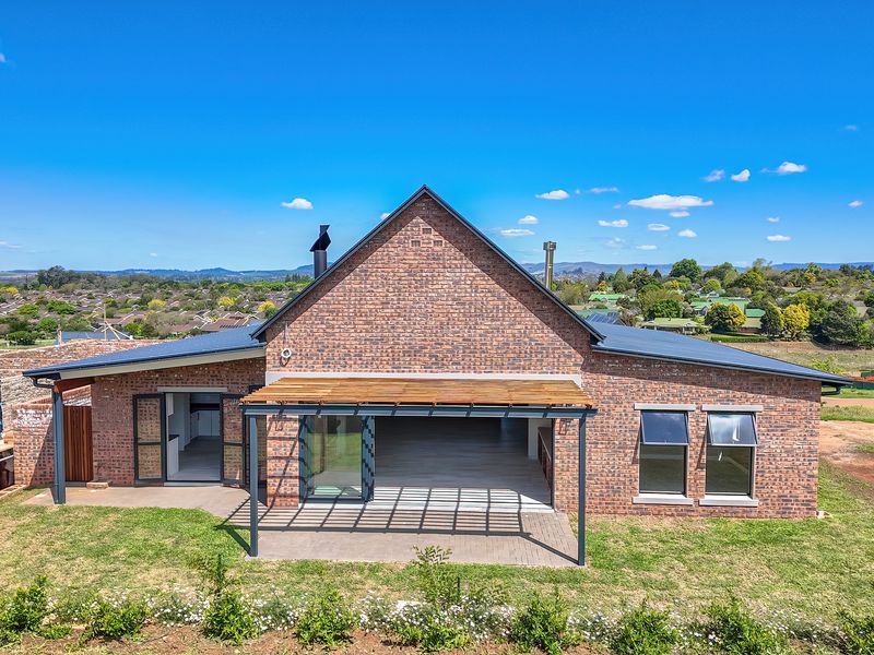 A rear view of a modern face brick house featuring a timber pergola, paved patio, and large sliding doors opening to the interior living space.