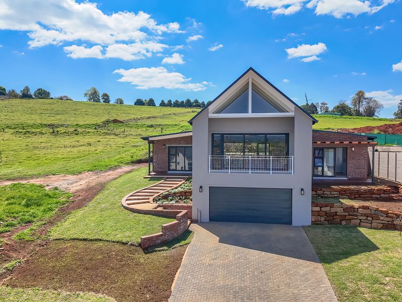 Modern double-story home featuring a gabled roof, integrated double garage, paved driveway, and a balcony overlooking a spacious rural landscape.