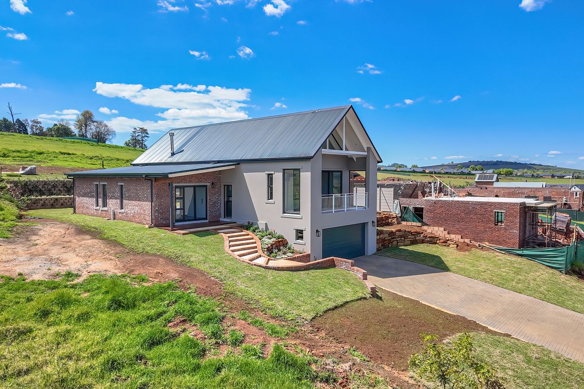 Modern double-story residence featuring a combination of brick and plastered finishes, a metal roof, an integrated garage, and a balcony overlooking the surrounding landscape.