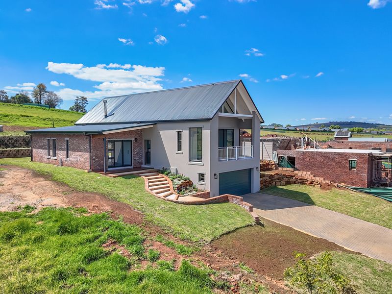 Modern double-story residence featuring a combination of brick and plastered finishes, a metal roof, an integrated garage, and a balcony overlooking the surrounding landscape.