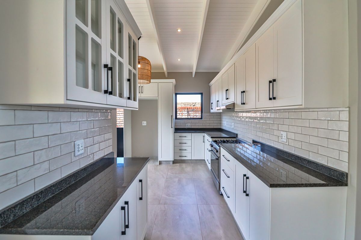 Modern galley-style kitchen featuring white shaker cabinetry, granite countertops, subway tile backsplash, and high-quality built-in appliances under an exposed beam ceiling.
