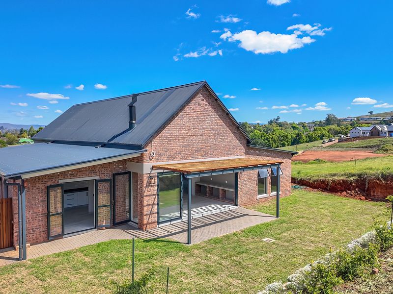 Rear view of a modern brick home featuring a covered patio with a timber pergola, built-in braai, and large sliding doors opening to the garden.