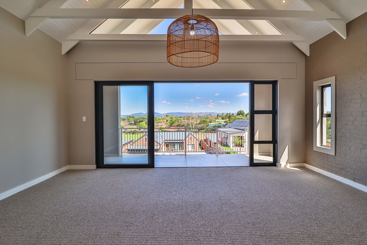 Spacious living area featuring a vaulted ceiling with exposed rafters, carpeted flooring, and large sliding doors opening onto a balcony with scenic views.