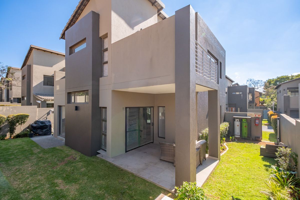 Rear view of a modern double-story house featuring a covered patio, balcony, and a well-maintained private garden area.