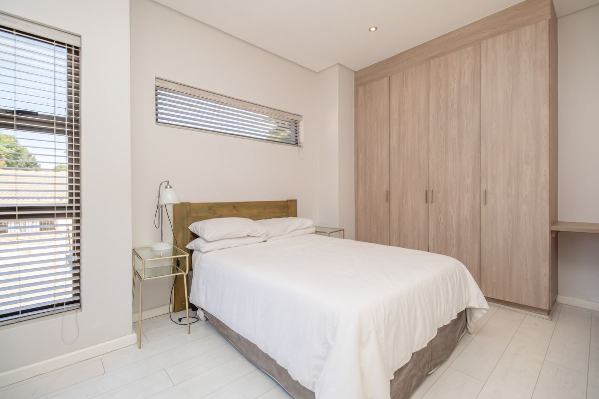 A bright, modern bedroom featuring light wood-toned built-in wardrobes, laminate flooring, and clean, neutral finishes.