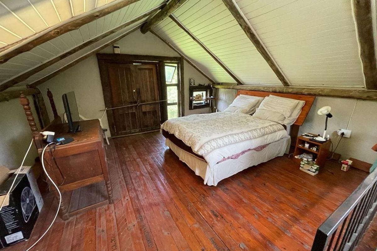 A rustic loft-style bedroom featuring exposed timber beams, vaulted ceilings, and polished wooden flooring with double door access.