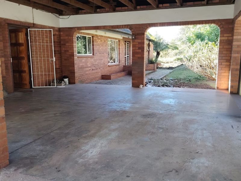 A spacious covered patio area featuring exposed timber roof trusses, brick pillars, and concrete flooring, offering direct access to the rear garden.