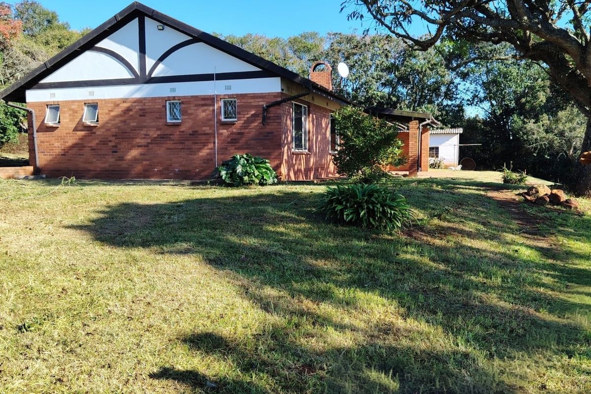 A view of the rear brick facade of the house, featuring a gabled roof, chimney, and established garden surroundings.