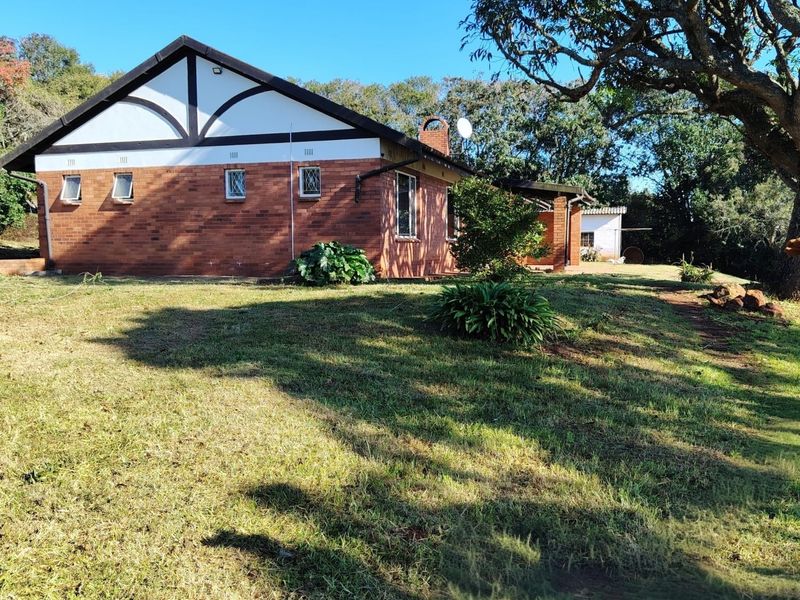 A view of the rear brick facade of the house, featuring a gabled roof, chimney, and established garden surroundings.