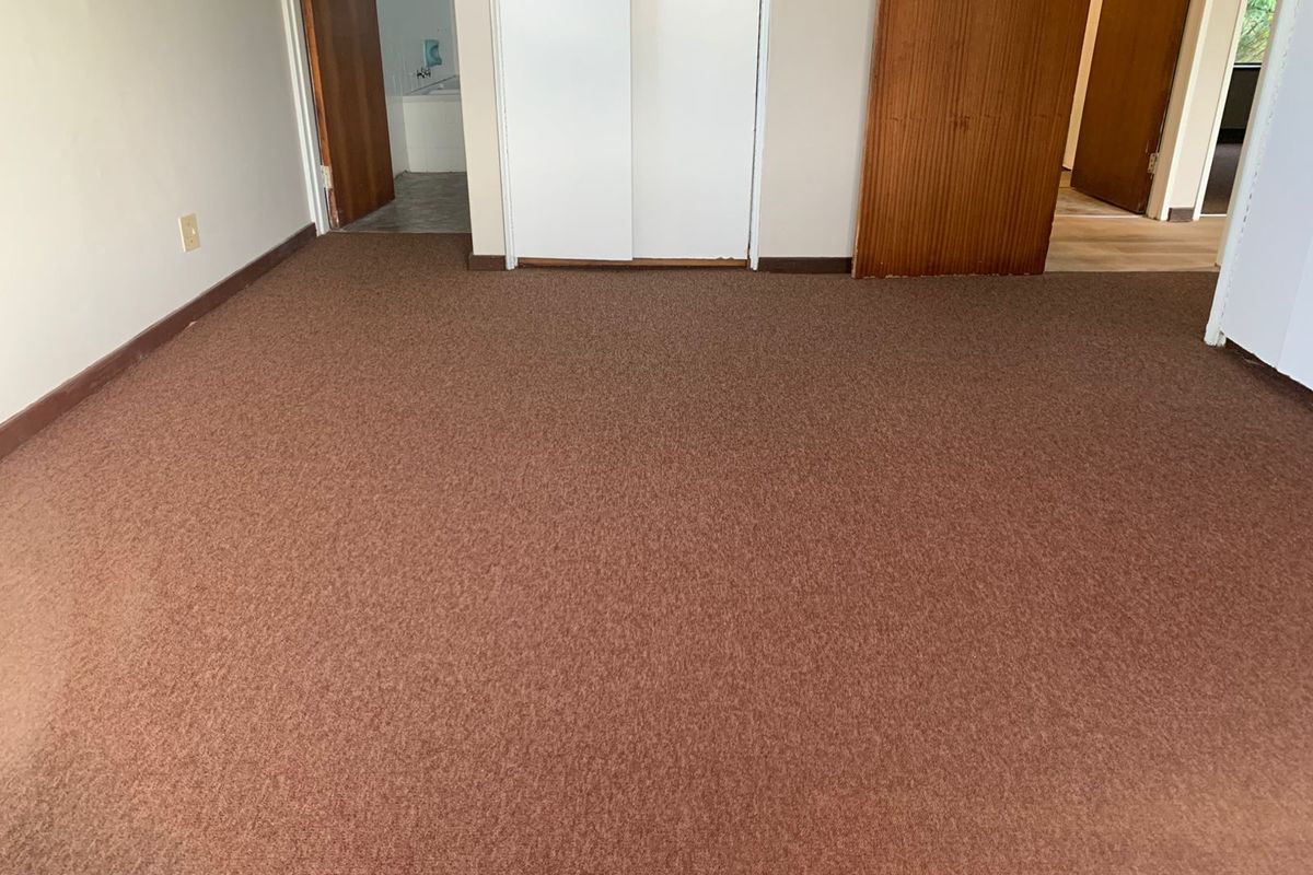 An empty bedroom featuring brown carpet flooring, built-in cupboards, and access to an adjoining bathroom.