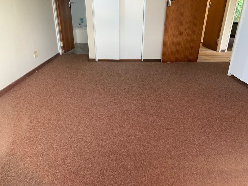 An empty bedroom featuring brown carpet flooring, built-in cupboards, and access to an adjoining bathroom.