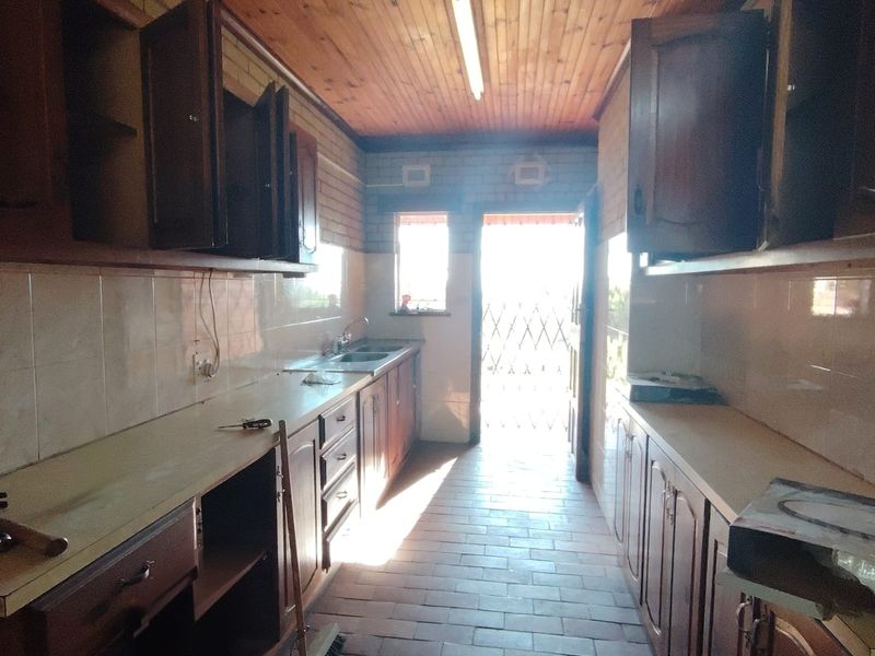 A dated galley-style kitchen featuring wooden cabinetry, tiled countertops, and a timber ceiling, requiring modernization to improve functionality and aesthetic appeal.