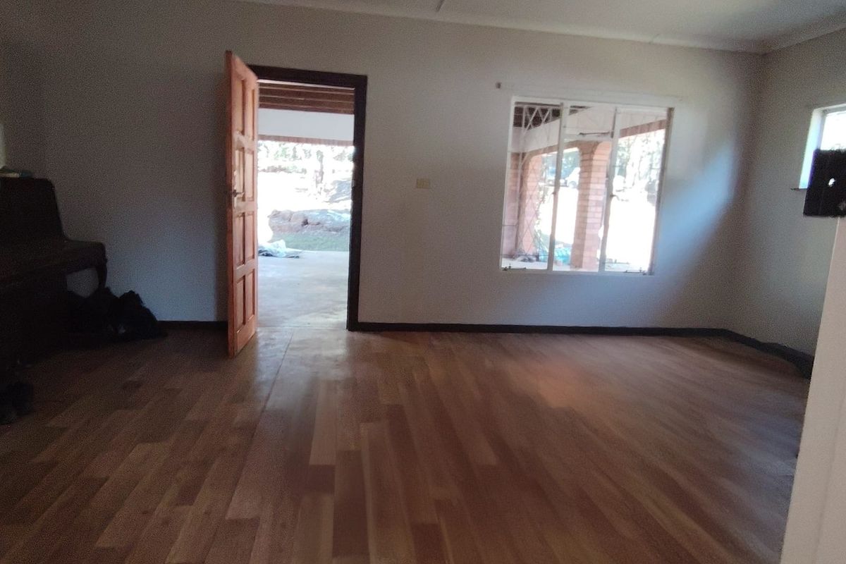 An empty living room featuring timber flooring, a wooden door leading to an outdoor area, and natural light from the windows.