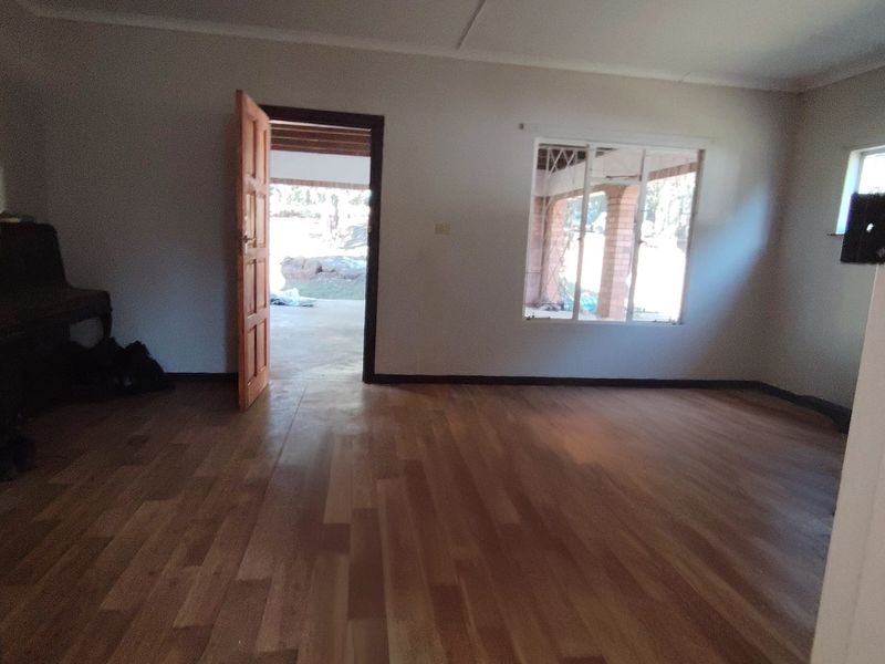 An empty living room featuring timber flooring, a wooden door leading to an outdoor area, and natural light from the windows.